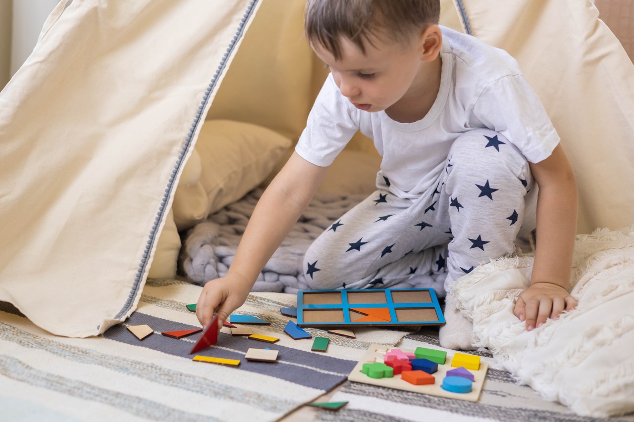 Menino em cabaninha brincando de jogo de montar com formas geométricas coloridas, simbolizando ausência de sintomas de sintomas de atraso desenvolvimento neuropsicomotor